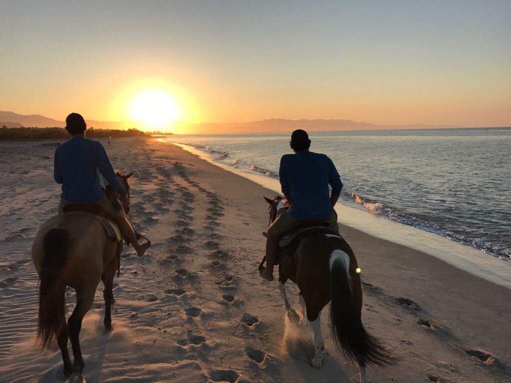 A couple riding horses on the beach at sunset on their East Cape, Baja vacation