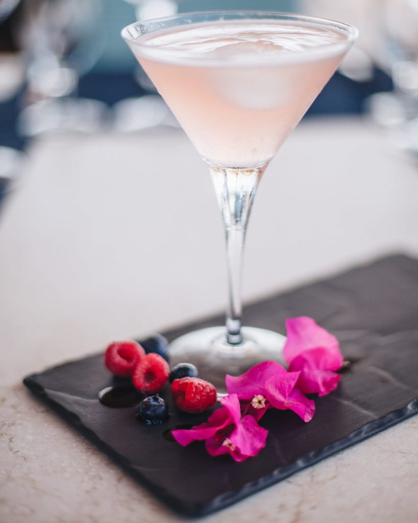 A Sea of Cortéz cocktail presented with fresh berries and bougainvillea flowers